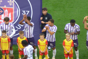 Eine Gruppe junger Jungs steht auf einem grünen Fußballfeld, klatscht in die Hände, mit einem Banner und Logos im Hintergrund.