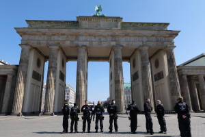 Eine Gruppe von Polizisten vor dem Brandenburger Tor in Berlin, Deutschland, ein Tor mit Säulen, eine Statue oben drauf und Gebäude mit Fenstern drumherum, unter einem sichtbaren Himmel.