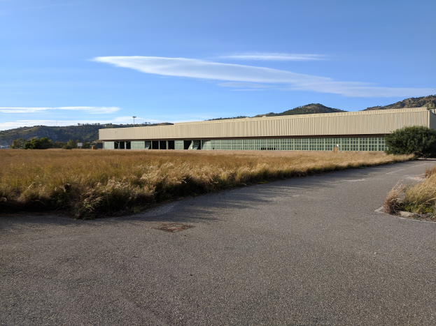 Leere Straße, die zu einem großen Gebäude in einem Feld führt, mit Hügeln und bewölktem Himmel im Hintergrund, identifiziert als Hauptquartier des San Francisco International Airport.