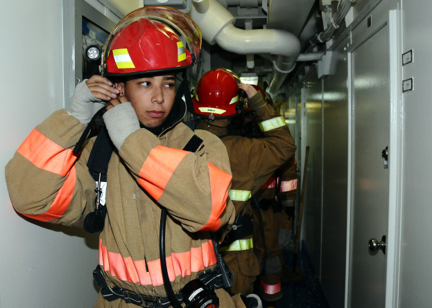 Gruppe von Feuerwehrleuten in Uniform, die zusammen in einem Raum mit Rohren und Equipment stehen, was auf eine Übung hinweist.