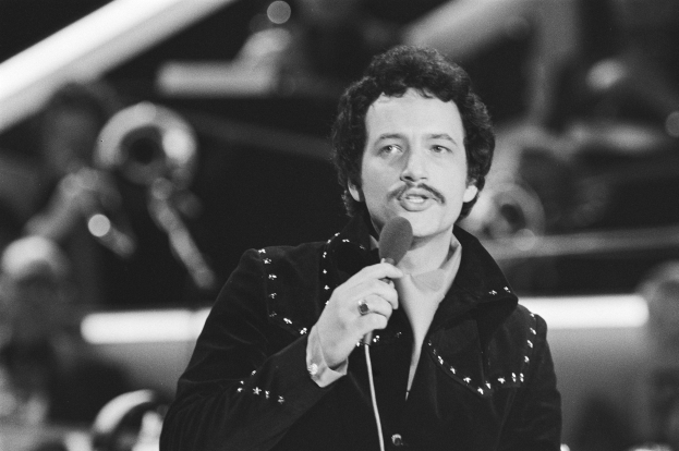 Ein als Elvis Presley identifizierter Mann hält ein Mikrofon während einer Live-Performance in einem Schwarz-Weiß-Foto mit unscharfem Hintergrund.