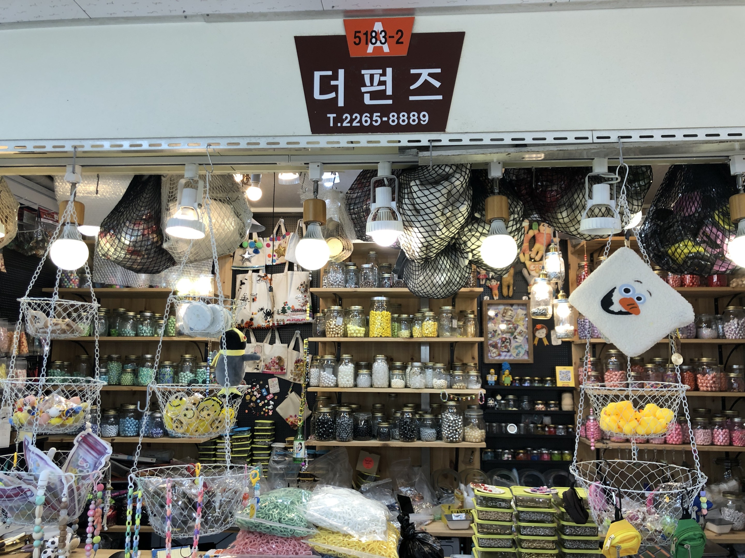 Ein Ladeneinrichtungsbild mit verschiedenen Gegenständen wie Körbchen, Lichtern, Flaschen und Spielzeugen auf Regalen, mit einem Schild öber dem Eingang, das es als bestes koreanisches Geschäft in Seoul ausweist.