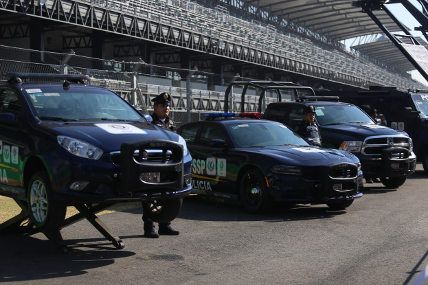 Eine Gruppe von Polizeiwagen vor einer Rennstrecke geparkt, mit uniformierten Beamten auf der Straße und einem Stadion im Hintergrund.