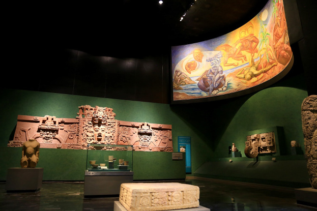 Ein Museumsraum mit verschiedenen Artefakten, darunter Skulpturen, Tischgegenstände, eine Texttafel, eine Wandmalerei und Deckenbeleuchtung im Mexiko-Stadt-Museum der Anthropologie.